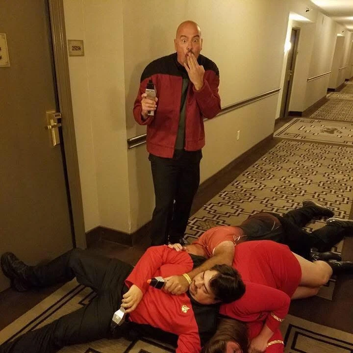 Mike Chinakos in a Starfleet-inspired uniform, reacting in mock shock to a chaotic scene in a hotel hallway